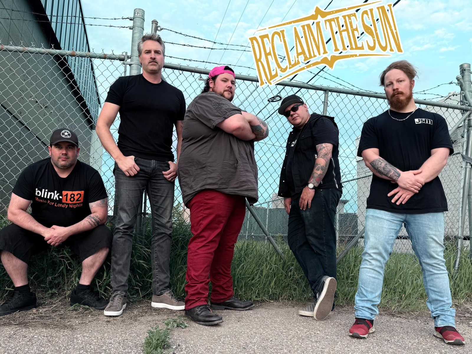 The band posed in front of a chain-link fence topped with barbed wire